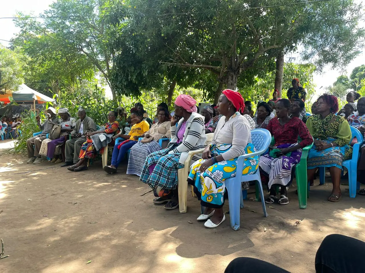 Community members seated under trees at a gathering