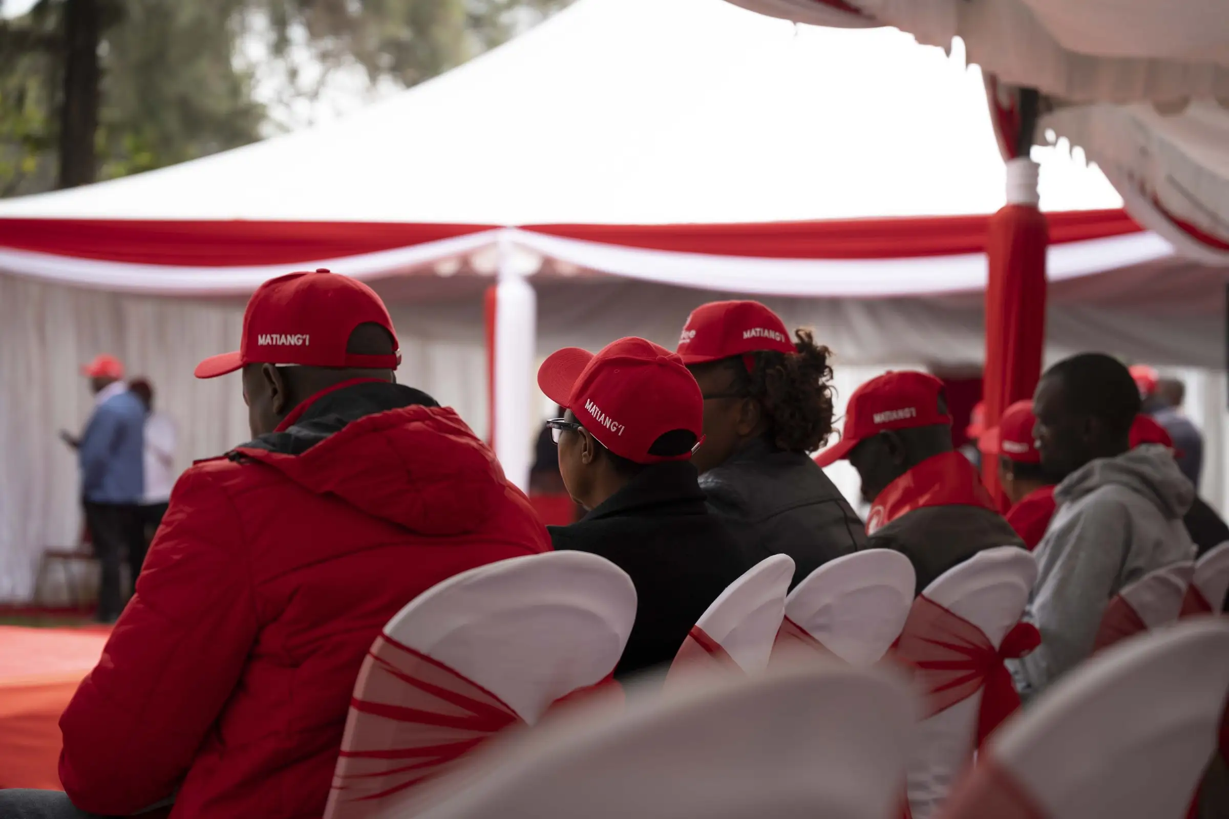 Supporters in red caps seated under a red and white tent