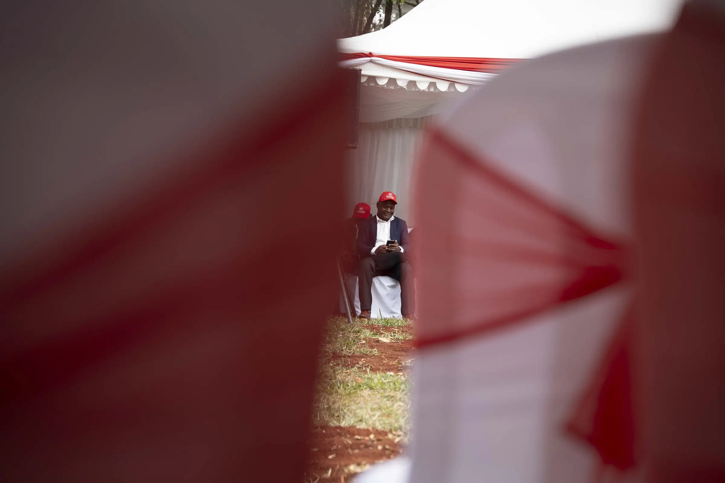 A supporter in a red cap seated at an event, framed by chairs