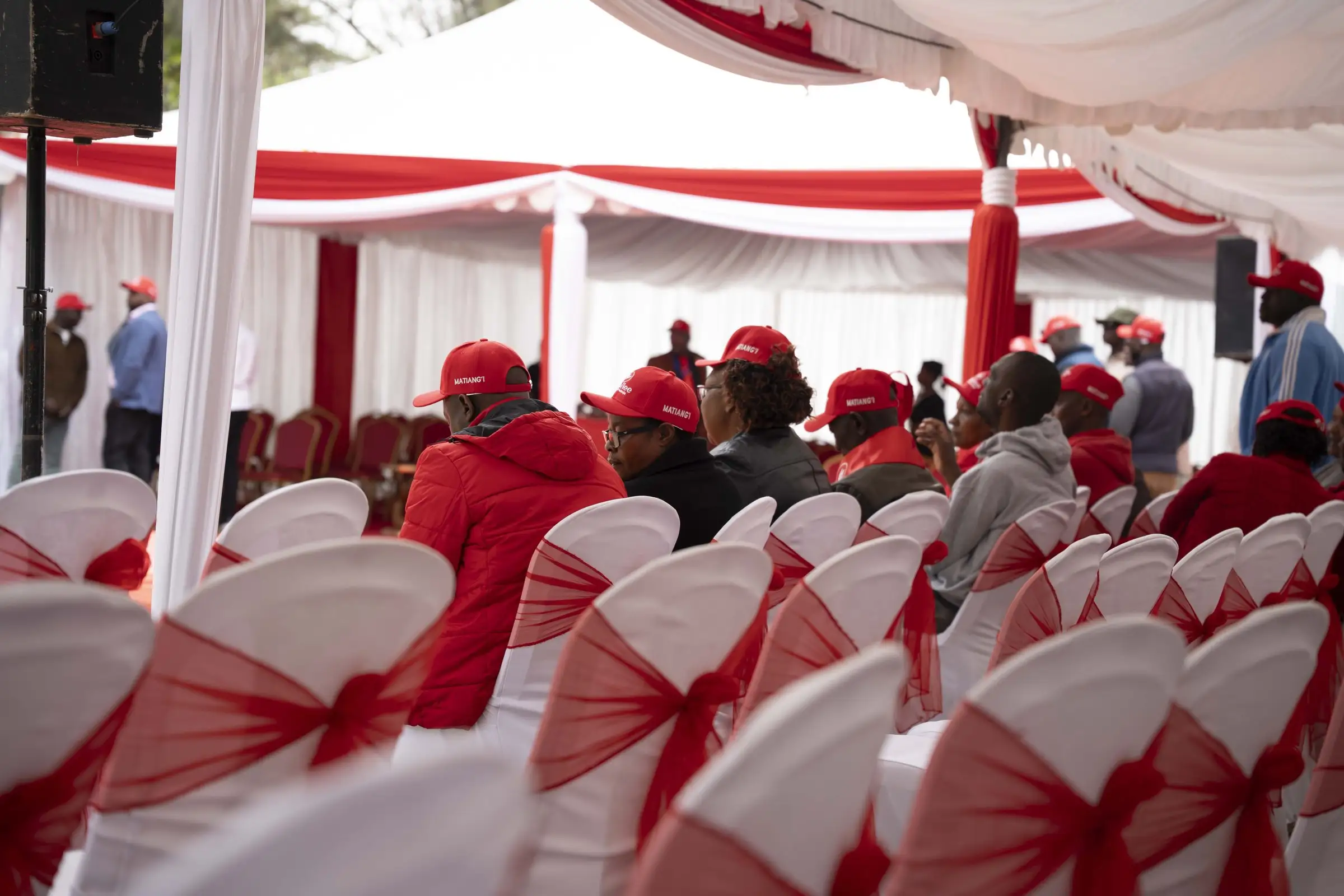 Rows of decorated chairs and supporters under a tent